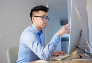 121513714-young-asian-male-programmer-wearing-shirt-and-glasses-working-while-sitting-in-front-of-desktop-comp