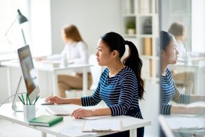 Profile view of pretty Asian programmer working on ambitious project while sitting in modern open plan office, waist-up portrait